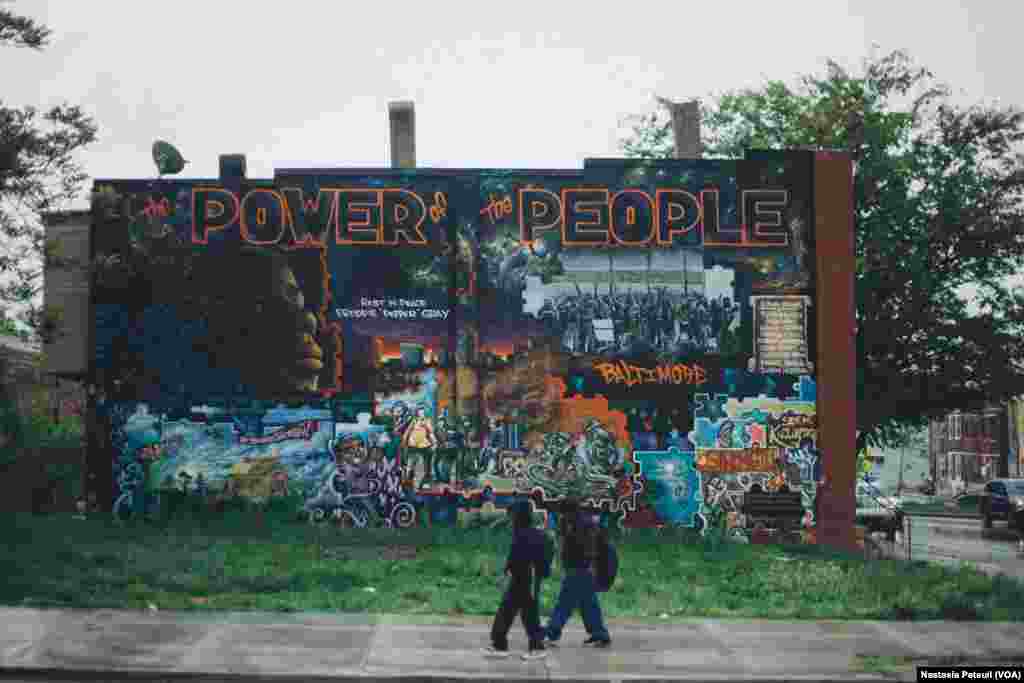 Des enfants du quartier marchent devant une autre fresque murale qui représente Freddie Gray avec le slogan "le pouvoir du peuple". Baltimore, le 6 mai 2016. (VOA/ Nastasia Peteuil)