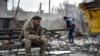 A Ukrainian serviceman smokes as a local resident clears debris near a building damaged in the Russian air raid in the town of Orikhiv, Zaporizhzhia region, Ukraine, April 5, 2024.
