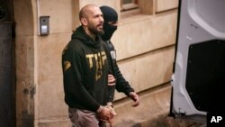 A police officer escorts Andrew Tate, center, handcuffed, from the Court of Appeal in Bucharest, Romania, March 12, 2024.