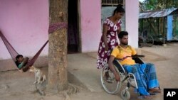 FILE - Thangarasa Kirubakaran, a former rebel fighter who was disabled in the civil war, gets help from his wife as he sits in a wheelchair outside his home in Mullaitivu, Sri Lanka, May 6, 2023. 