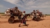 A Sudanese woman, who fled the conflict in Murnei in Sudan's Darfur region, walks beside carts carrying her family belongings upon crossing the border between Sudan and Chad in Adre, Chad, Aug. 2, 2023. 