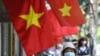 FILE - Women walk past Vietnam national flags hoisted along a street in Hanoi on May 18, 2020. Concern is growing over a purported internal Vietnamese directive which is said to order government agencies to increase surveillance of citizens and crack down on civil society.