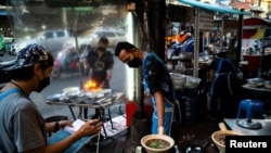 Sejumlah pedagang jajanan kaki lima tampak mengenakan masker sebagai proteksi melawan penyebaran COVID-19 ketika berjualan di area pecinan di Bangkok, Thailand, pada 17 Maret 2022. (Foto: Reuters/Athit Perawongmetha)
