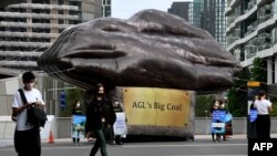 Morning commuters walk past a giant inflatable depicting a piece of coal erected by Greenpeace outside Australian energy company AGL in Melbourne on March 28, 2022. 
