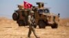FILE - A U.S. soldier walks past a Turkish armored vehicle during the first joint ground patrol of American and Turkish forces in the so-called "safe zone" on the Syrian side of the border with Turkey, near Tal Abyad, Syria, Sept. 8, 2019.