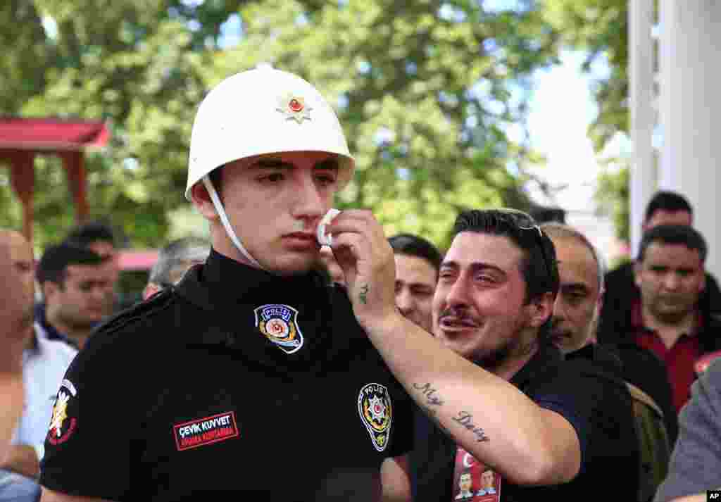 A relative, right, of one of the victims of explosion, wipes the face of a Turkish police officer, serving as a honor guard, during the funeral procession for two of the victims at Fatih mosque in Istanbul.