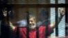 FILE - Former Egyptian President Mohammed Morsi, wearing a red jumpsuit that designates he has been sentenced to death, raises his hands inside a defendants cage in a makeshift courtroom at the national police academy, in an eastern suburb of Cairo.
