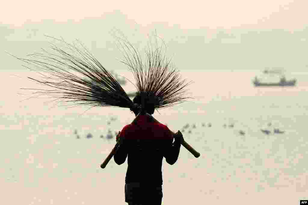 Seorang pekerja India membawa sepasang sapu ketika membersihkan Sangam, lokasi pertemuan tiga Sungai Gangga, Yamuna dan Saraswati, menjelang festival tahunan Magh Mela di Allahabad.