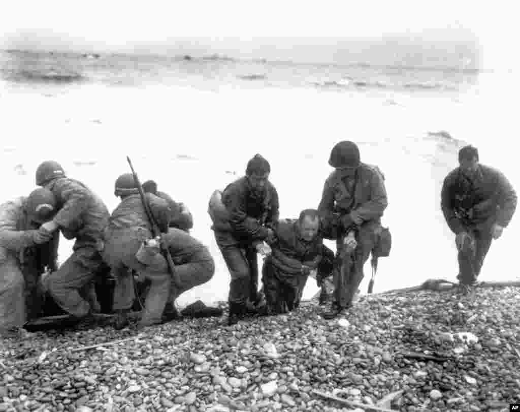 Members of an American unit reach Utah Beach on a life raft after their landing craft was hit and sunk by German coastal defenses. Here soldiers help their exhausted comrades ashore during the Normandy invasion, June 6, 1944.&nbsp;