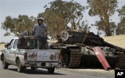 Des rebelles libyens passant près d'un tank gouvernemental détruit par l'OTAN