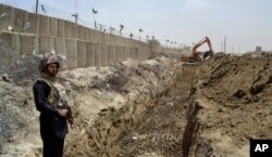 FILE - In this May, 16, 2014 file photo, a Pakistani border guard stands alert as an excavator digs a trench along Pakistan Afghanistan border at Chaman post in Pakistan.