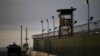 FILE - A U.S. soldier stands in the turret of a vehicle with a machine gun, left, as a guard looks on from a tower at the Guantanamo Bay prison in Cuba.