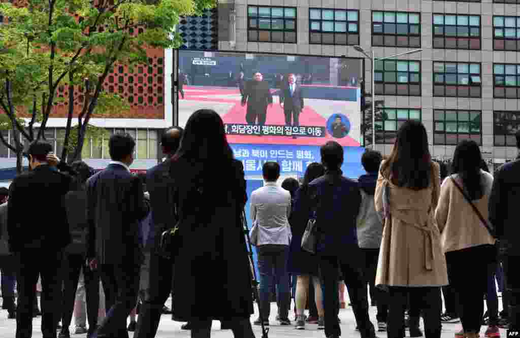 Des gens regardent en direct le président sud-coréen Moon Jae-in en train de marcher avec le dirigeant nord-coréen Kim Jong Un dans la zone démilitarisée, sur un écran à Séoul le 27 avril 2018.