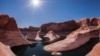 A houseboat sits in the green water and high orange cliffs of Lake Powell. The dramatic curves of Reflection Canyon show the path the river once took before Lake Powell. (Photo: NPS / Gary Ladd)