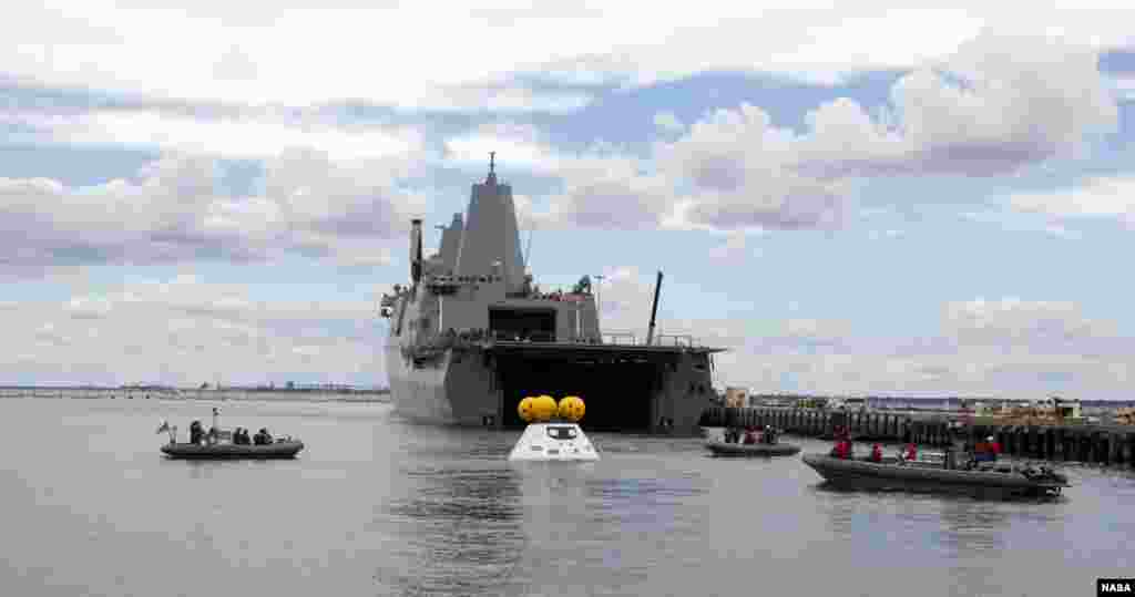 Seiring dengan merapatnya kapal USS Arlington milik Angkatan Laut AS di dermaga Angkatan Laut Norfolk di Virginia, para penyelam dalam perahu-perahu kecil mendekati versi uji Orion NASA dalam uji pemulihan stasioner. Pengujian ini membantu untuk memastikan kapan Orion kembali dari misi-misi luar angkasa dan jatuh di Samudera Pasifik.