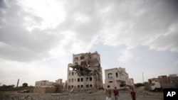 Warga berdiri di dekat sebuah gedung yang hancur akibat serangan udara pimpinan Saudi di Sana'a, Yaman (6/7). 