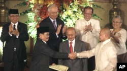 Negosiator perdamaian pemerintah Filipina Marvic Leonen (kanan) dan pemimpin negosiator Front Pembebasan Islam Moro (MILF) Mohagher Iqbal (kiri) berjabat tangan seusai menukar dokumen kesepakatan perdamaian di istana Malacanang, Manila, Filipina (15/10). 