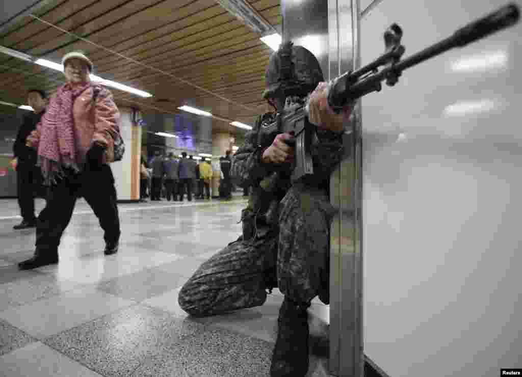 Seorang tentara Korea Selatan siaga di sebuah stasiun kereta bawah tanah, sementara seorang wanita melihat aksi tersebut, selama latihan anti-teror di Seoul.