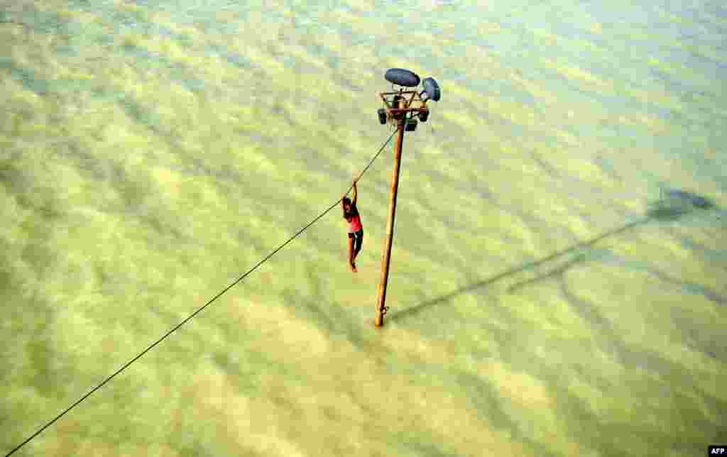 Seorang pemuda India bergelantungan di kawat listrik sebelum terjun ke air bah yang meluap dari sungai Gangga Ganges di Allahabad, 6 Agustus 2013. 