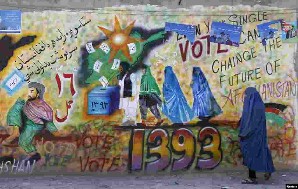 Seorang perempuan berjalan melewati grafiti yang mendorong masyarakat untuk memberikan suaranya di provinsi Kandahar, Afghanistan (30/3).&nbsp;(Reuters/ Ahmad Nadeem)