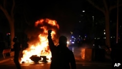 A protestors raises his fist at police across a burning barricade during clashes between protestors and police in Barcelona, Spain, Tuesday, Oct. 15, 2019.