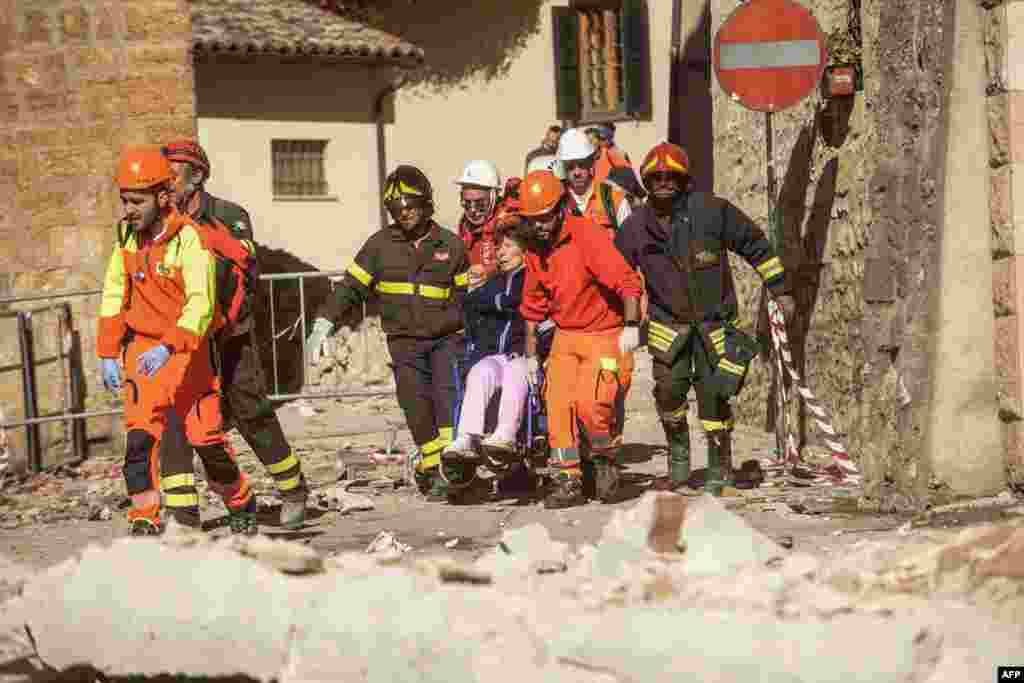 Para petugas medis membawa seorang perempuan di kursi roda yang selamat dari gempa 6,6 skala Richter di Norcia, Italia.