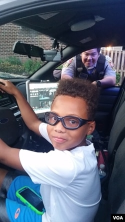 A boy gets a look inside a police car with Sergeant John Kim watching during National Night Out in Fairfax Country, Virginia, Aug. 2, 2016. (D. Block/VOA)
