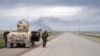 Smoke billows in the background as Kurdish Peshmerga fighters take positions on the side of a road in the northern Iraqi city of Kirkuk, Jan. 30, 2015.