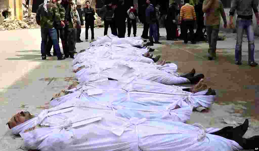 Syrians stand next to dead bodies that have been pulled from the river near Aleppo, March 10, 2012.