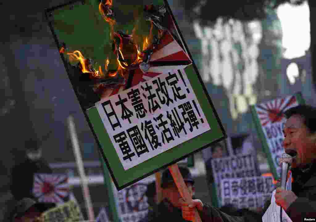 A protester from a right-wing, conservative and anti-Japanese civic group chants slogans denouncing Japanese PM Shinzo Abe&#39;s visit to the Yasukuni Shrine as he holds a placard that has been set alight, in front of the Japanese Embassy in Seoul.