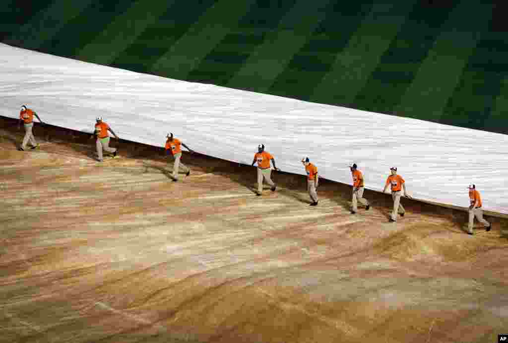 Para penjaga lapangan memindahkan terpal dari lapangan saat penundaan pertandingan karena hujan antara permainan pertama dan kedua bisbol doubleheader antara Baltimore Orioles dan Pittsburgh Pirates, Kamis, 1 Mei 2014, di Maryland. 