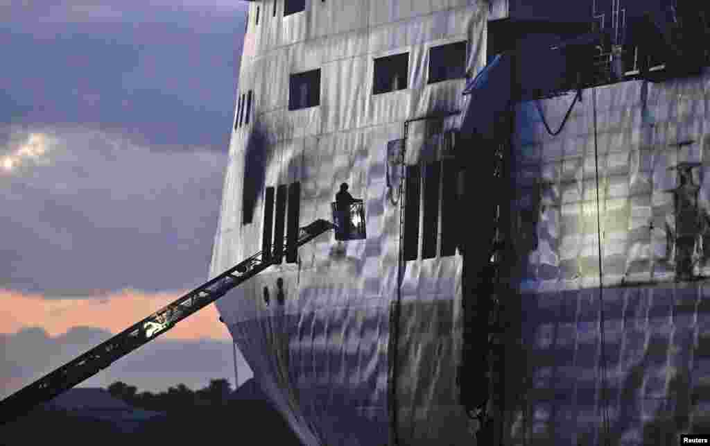 Firefighters stand on a ladder to inspect the Norman Atlantic multi-deck car-and-truck ferry docked at Brindisi harbor. Tugboats hauled the burnt-out hulk of the ferry that caught fire on Sunday off the coast of Greece into the southern Italian port on Friday, opening the way for an investigation into the cause of the blaze that killed at least 11 people.