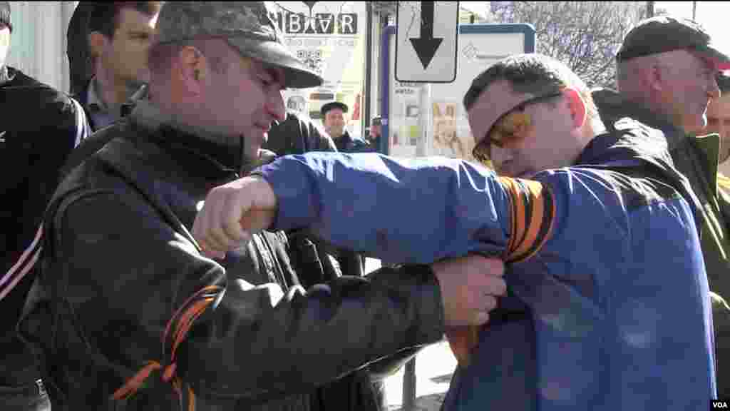 Seorang pria dengan mengikatkan pita pro-Rusia pada pria lain yang bergabung dengan kelompok "Pertahanan Diri" di luar parlemen di Simferopol (3/3). (Sebastian Meyer/VOA)