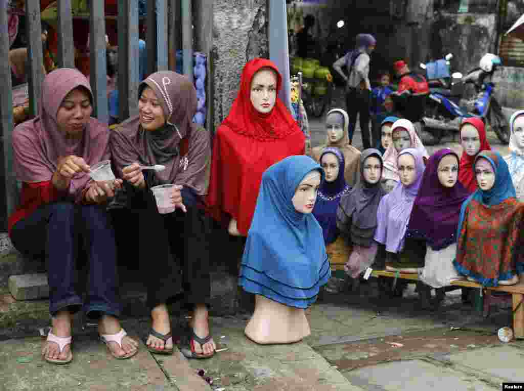 Dua gadis remaja duduk di dekat mannequin yang dipasangi jilbab untuk dijual di Pasar Tanah Abang, menjelang bulan suci Ramadan, di Jakarta, Indonesia.