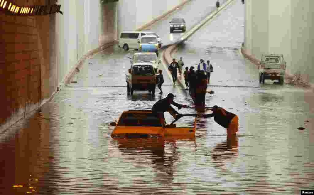 Seorang laki-laki yang mobilnya terperangkap dalam banjir di terowongan dibantu seorang laki-laki lainnya di Sana&#39;a, Yaman.