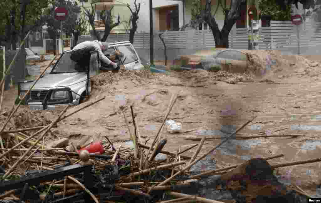 Seorang perempuan diselamatkan dari banjir oleh seorang warga yang berdiri di atas mobilnya dalam hujan deras di Chalandri, sebelah utara Athena, Yunani, 22 Februari 2013.