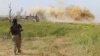 FILE - An Islamist rebel fighter walks by as smoke rises after what activists said was an airstrike by forces of Syria's President Bashar al-Assad at Qarmeed camp, after Islamist rebel fighters took control of the area, April 2015. 