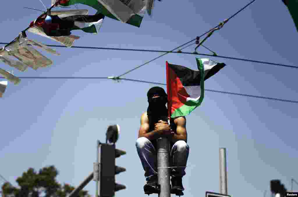 Seorang pemuda Palestina bertopeng duduk di atas tiang saat menyaksikan upacara pemakaman Mohammed Abu Khudair, 16, di Shuafat, pinggiran kota Arab di Yerusalem (4/7). (Reuters/Finbarr O&#39;Reilly)