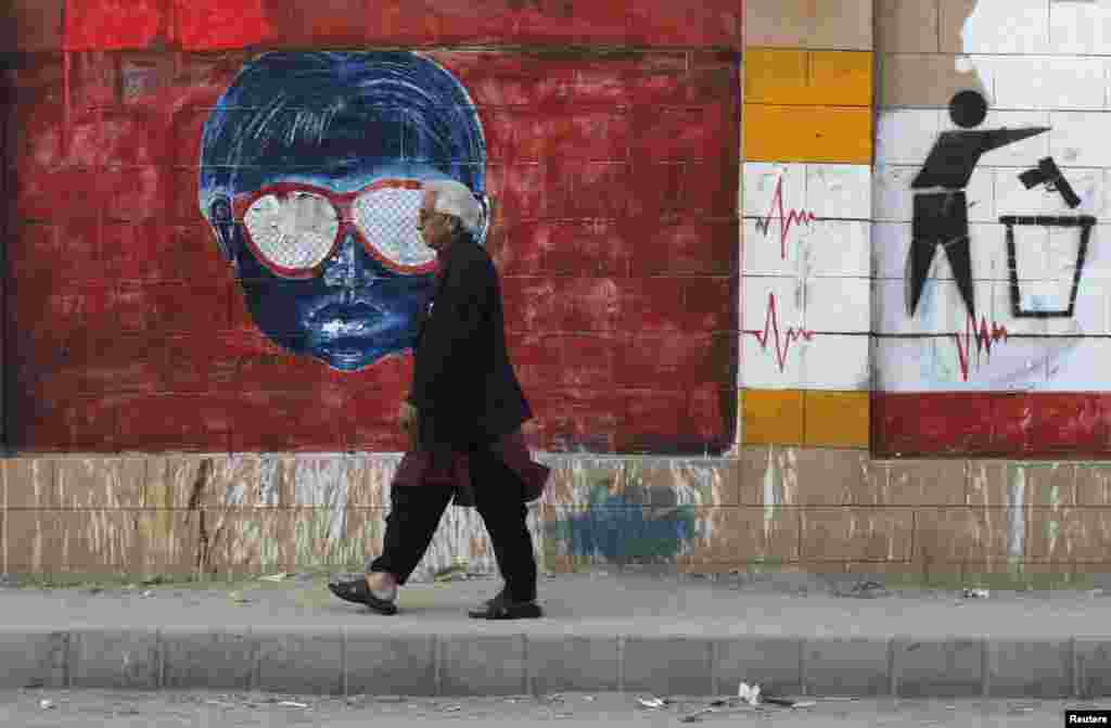 Seorang laki-laki berjalan melewati tembok berhiaskan grafiti yang dilukis oleh berbagai seniman untuk mempromosikan perdamaian, di sepanjang trotoar di Karachi, Pakistan.