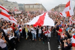 Demonstrators carry a huge historical flag of Belarus as thousands gather for a protest at the Independence square in Minsk, Belarus, Aug. 23, 2020.