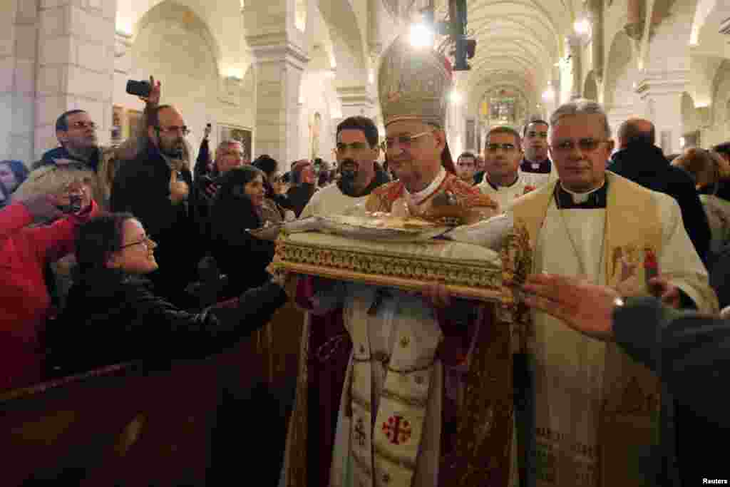 The Latin Patriarch of Jerusalem Fouad Twal (2nd R) carries a statuette of baby Jesus during Christmas midnight mass at the Church of St. Catherine, which is connected to the Church of the Nativity, in the West Bank town of Bethlehem. 