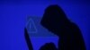 FILE - A hooded man holds a laptop computer as blue screen with an exclamation mark is projected on him in this illustration picture taken on May 13, 2017.
