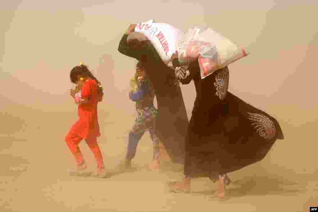 Displaced Iraqis, who fled the government's operation against the Islamic State (IS) group in the city of Fallujah, carry basic food items in a sand storm in a camp in Khaldiyeh, June 20, 2016.