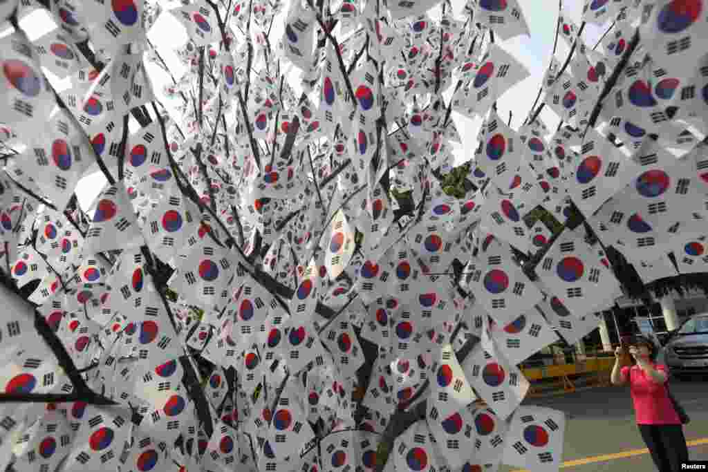 Seorang perempuan mengambil foto pohon dihiasi dengan bendera nasional di pemakaman nasional di Seoul pada hari peringatan pahlawan yang gugur di Korea Selatan.