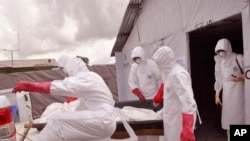 FILE - Health workers wearing protective gear remove the body of a man they suspect died from the Ebola virus at a treatment center on the outskirts of Monrovia, Liberia, Nov. 28, 2014.