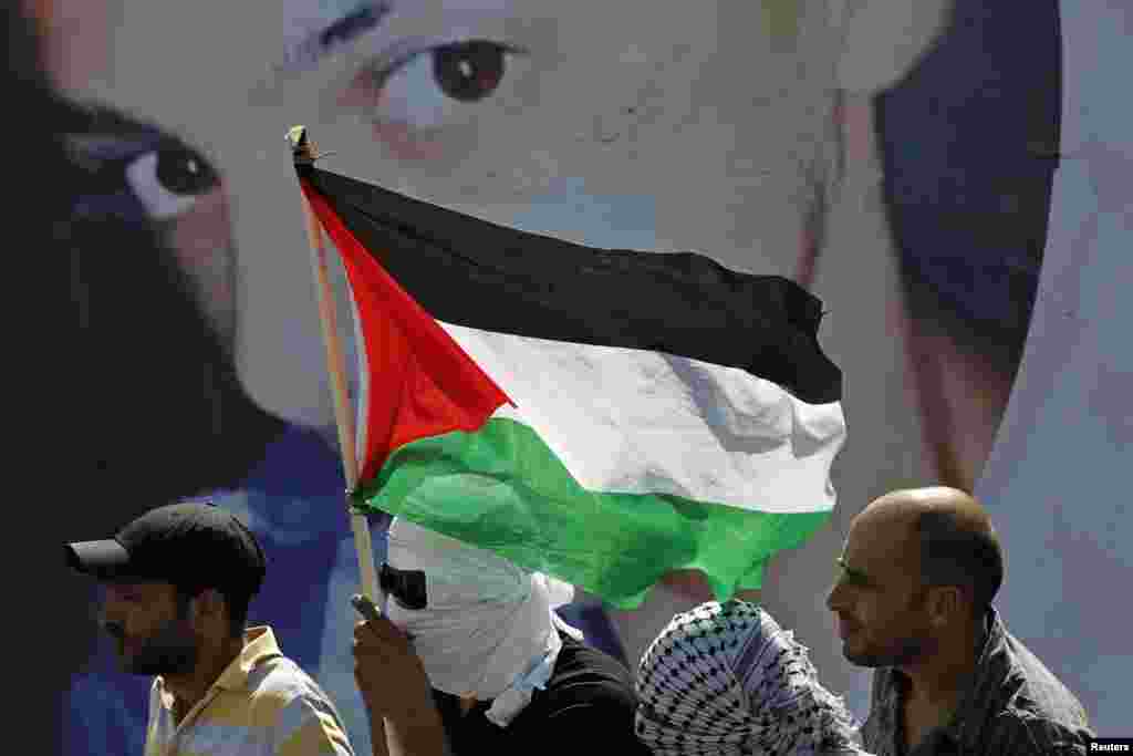 Warga Palestina berdiri di depan poster bergambar Mohammed Abu Khudair, 16, dalam pemakamannya di Shuafat, pinggiran kota Arab di Yerusalem (4/7). (Reuters/Finbarr O&#39;Reilly)