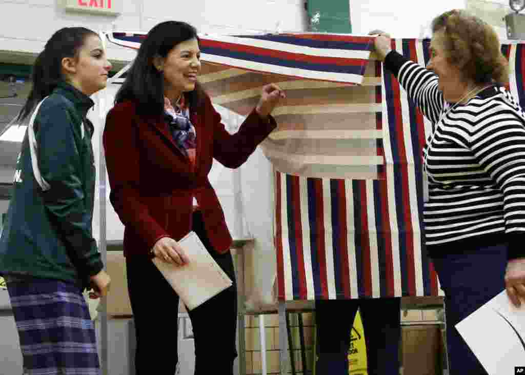 A poll worker lifts the curtain as Sen. Kelly Ayotte, R-N.H., center, leaves the voting booth with her daughter, Kate, Nov. 8, 2016, at Charlotte Avenue Elementary School in Nashua, N.H. 