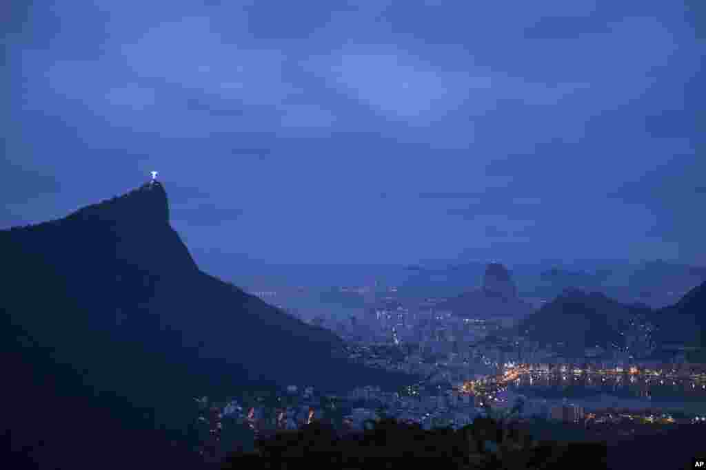 The Christ the Redeemer statue stands atop the Corcovado Mountain, left, at dawn in Rio de Janeiro, Brazil. The Lagoa Rodrigo de Freitas, seen illuminated at right, will host the rowing and canoe sprint events. 
