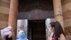 FILE - People wearing face masks stand outside the damaged entrance of the Association of Banks, in Beirut, Lebanon, Aug. 21, 2020.