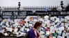 A woman passes a fence outside Brooklyn's Green-Wood Cemetery adorned with tributes to victims of COVID-19, Thursday, May 28, 2020, in New York. The memorial is part of the Naming the Lost project which attempts to humanize the victims who are often…